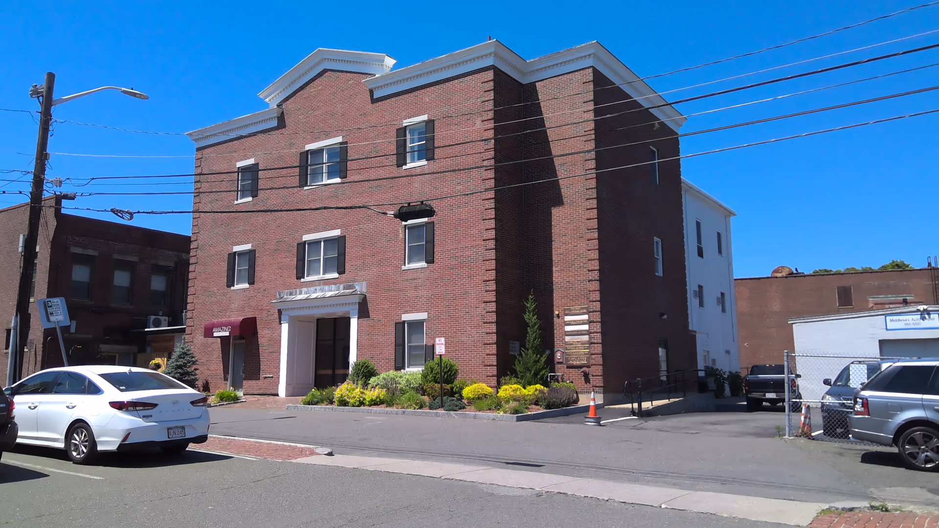 Brick senior living facility front facade with landscaping and parked cars along the street.