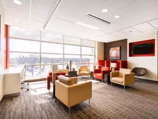 Bright lounge area with colorful chairs, a TV, and large windows.