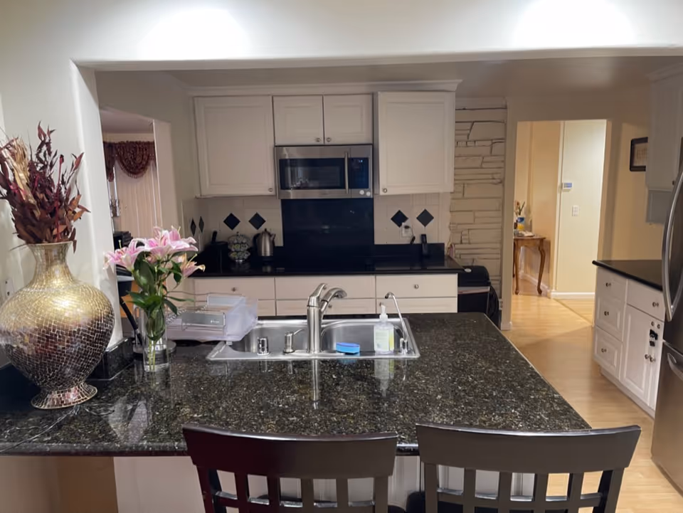 Open kitchen with granite island, white cabinets, stainless steel appliances, and bar stools.