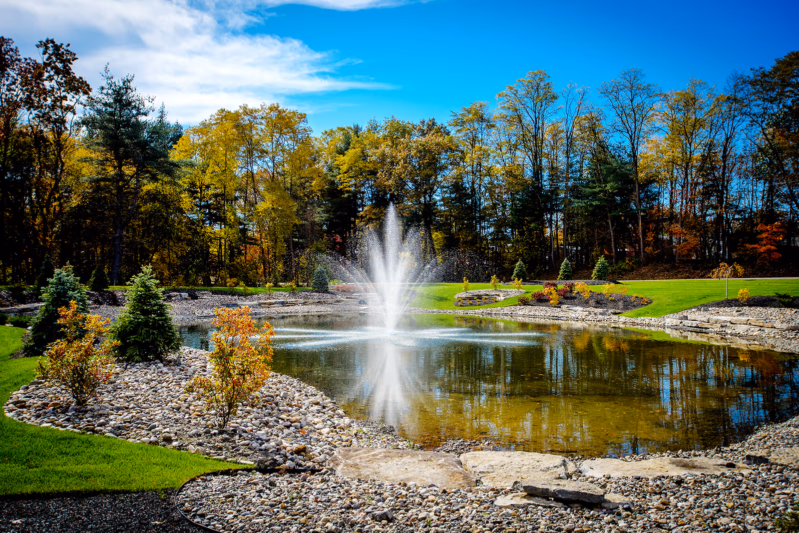 A landscaped pond with a central fountain, trees, and manicured lawns.