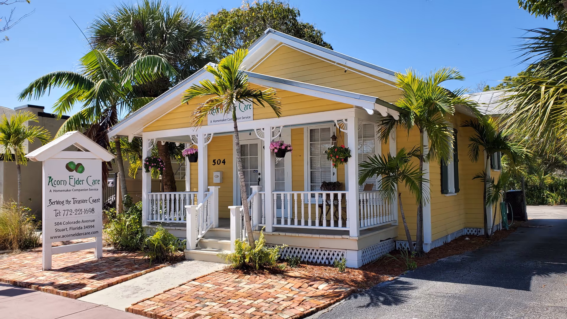 Yellow cottage-style elder care home with a welcoming front porch and palm trees.