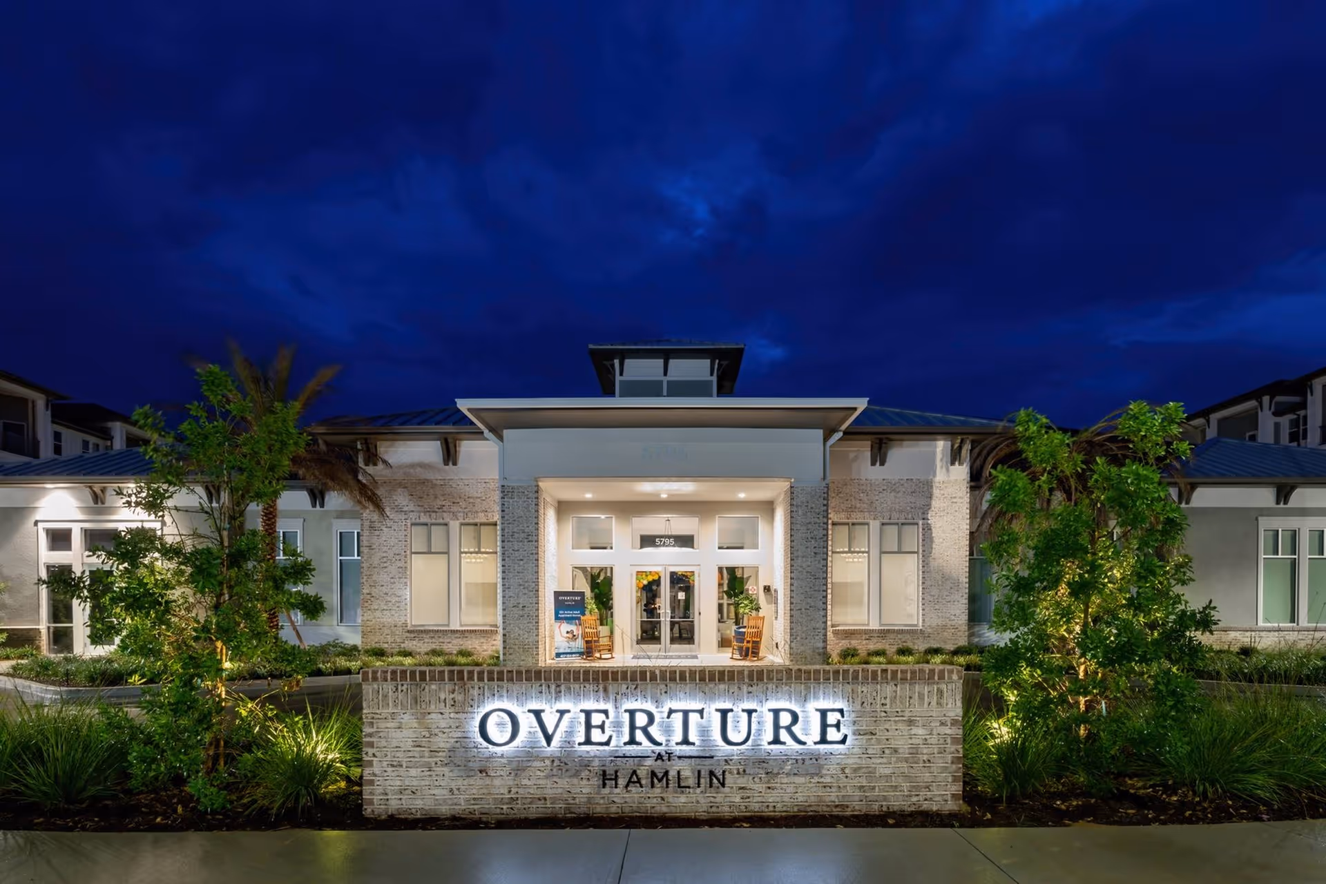 Front entrance of the Overture Hamlin building lit at night with an illuminated sign and surrounding landscaping.