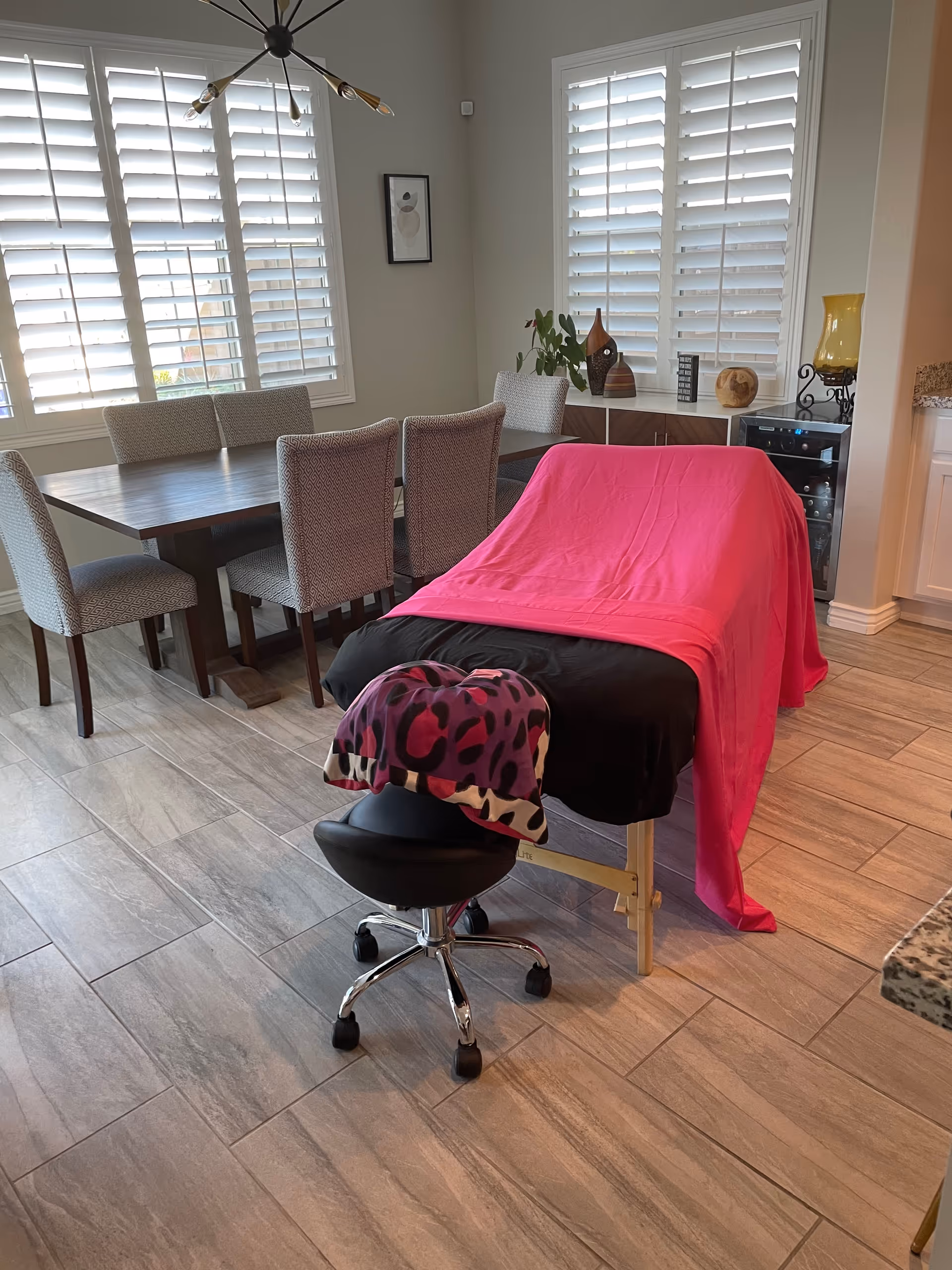A therapy table draped in pink sits beside a dining table in a bright room.