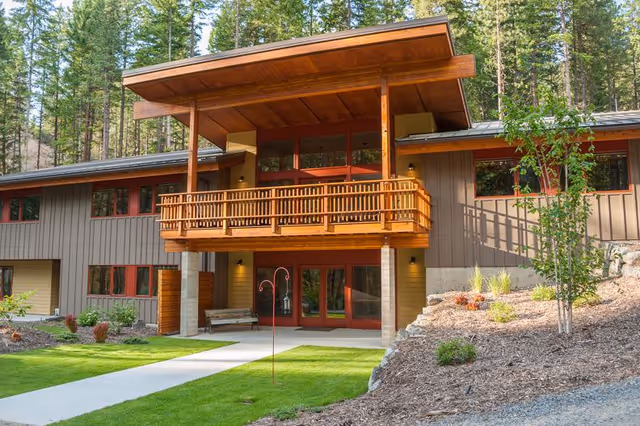 Modern wood-clad senior living building with a covered balcony and landscaped yard.
