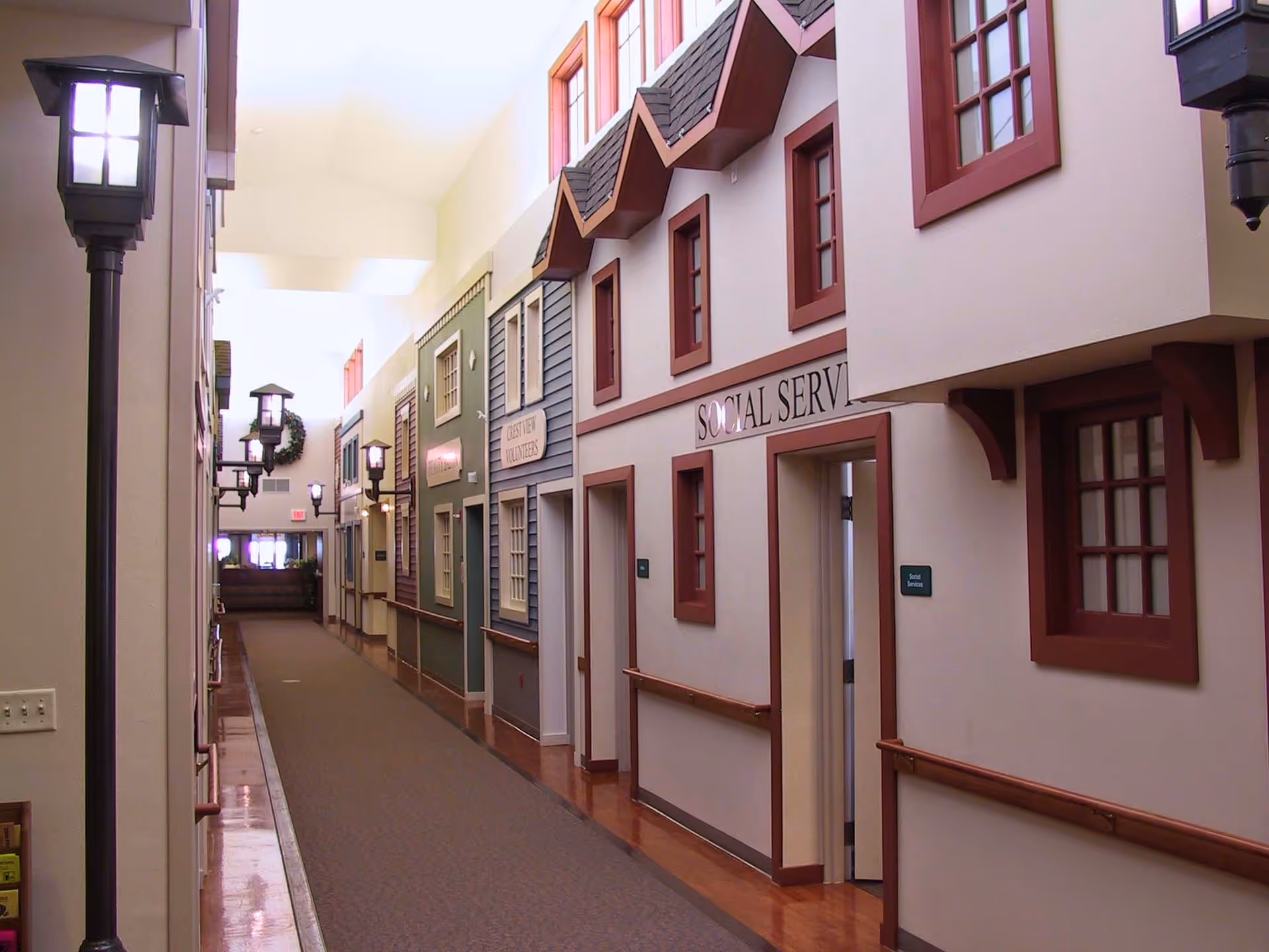 Indoor corridor of a senior living facility with doors, windows, and wall lamps.