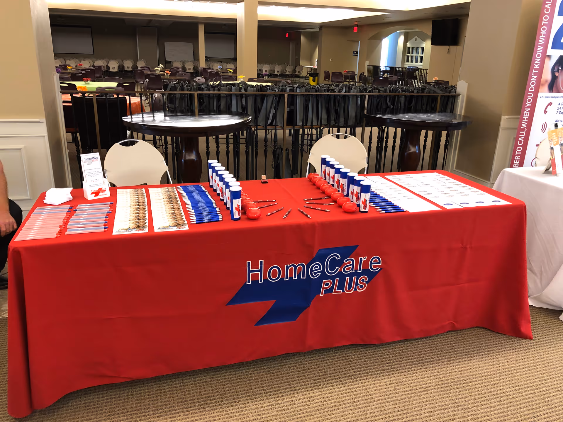 Red-covered registration table with HomeCare Plus branding, name tags, and pens in a lobby.