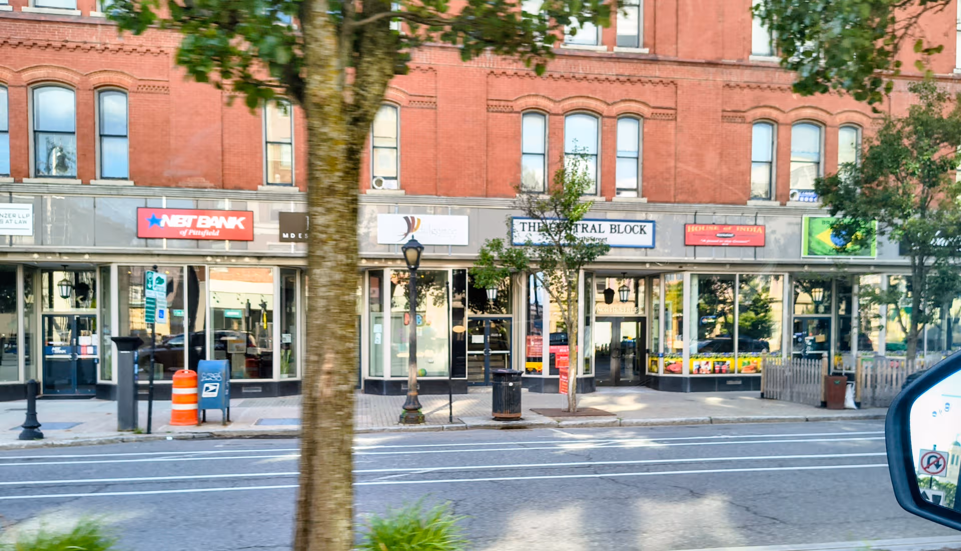 Brick building storefronts line a city street with signs and trees.