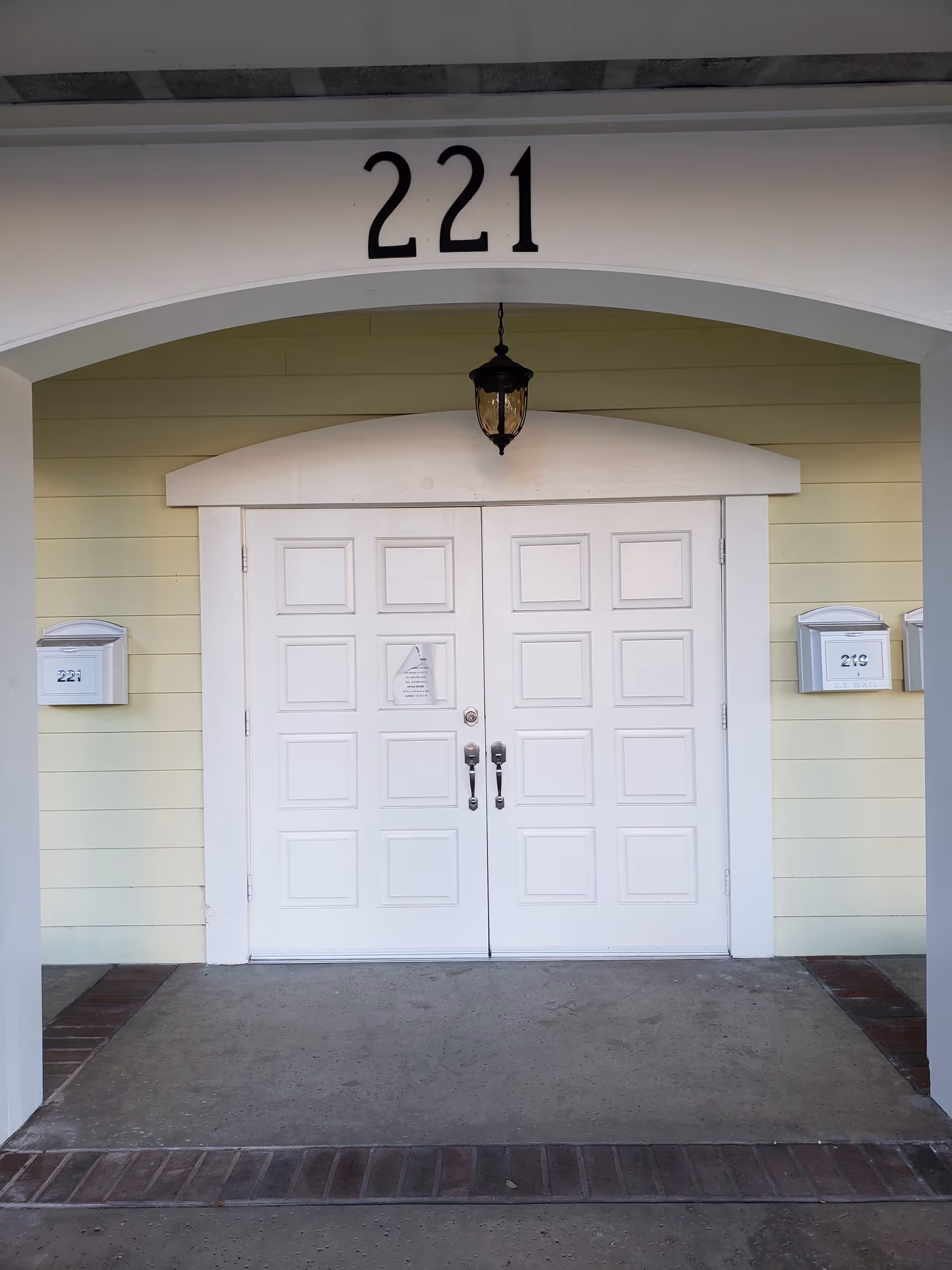 White double doors under a curved arch with a lantern light and the number 221.