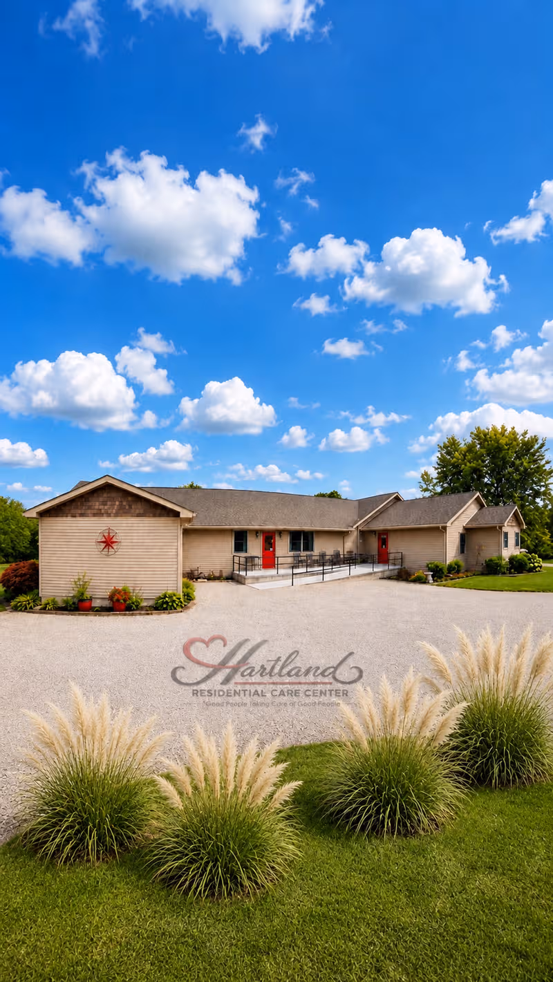 Single-story care center building with red doors, gravel driveway, and manicured landscaping under blue sky.