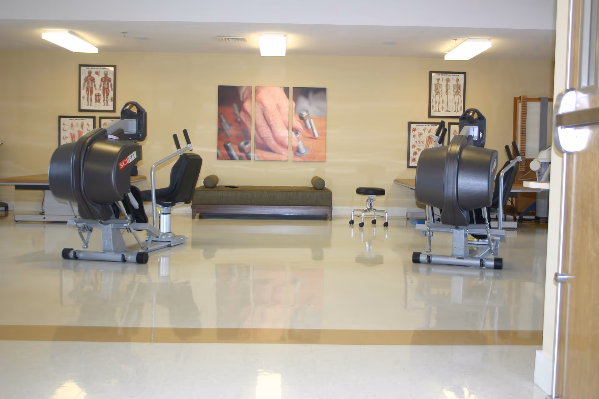 Rehabilitation/exercise room with cardio/strength machines, a bench, and anatomical charts on the wall.