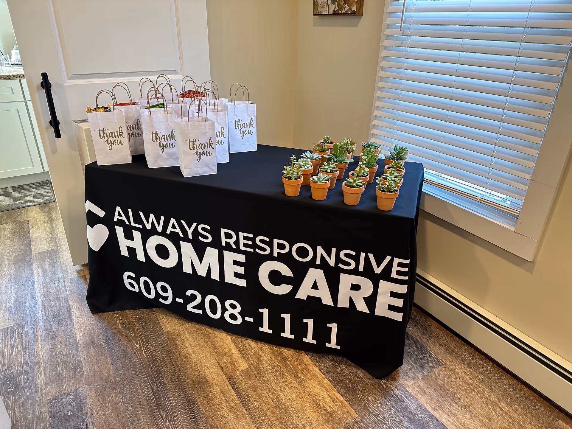 Table with branded cover, gift bags, and potted succulents in an interior room.