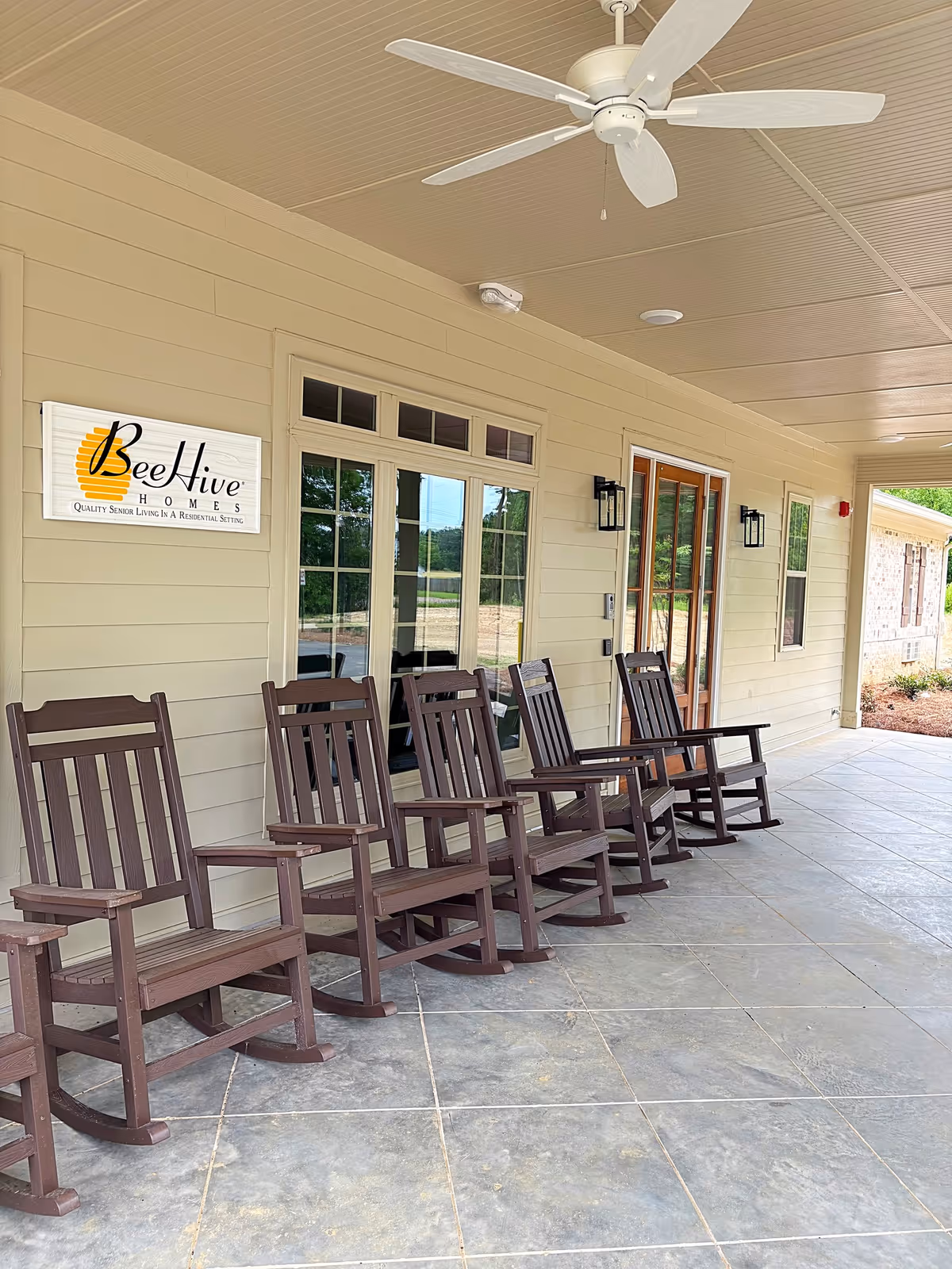 A covered outdoor patio with brown rocking chairs along the BeeHive Homes sign.