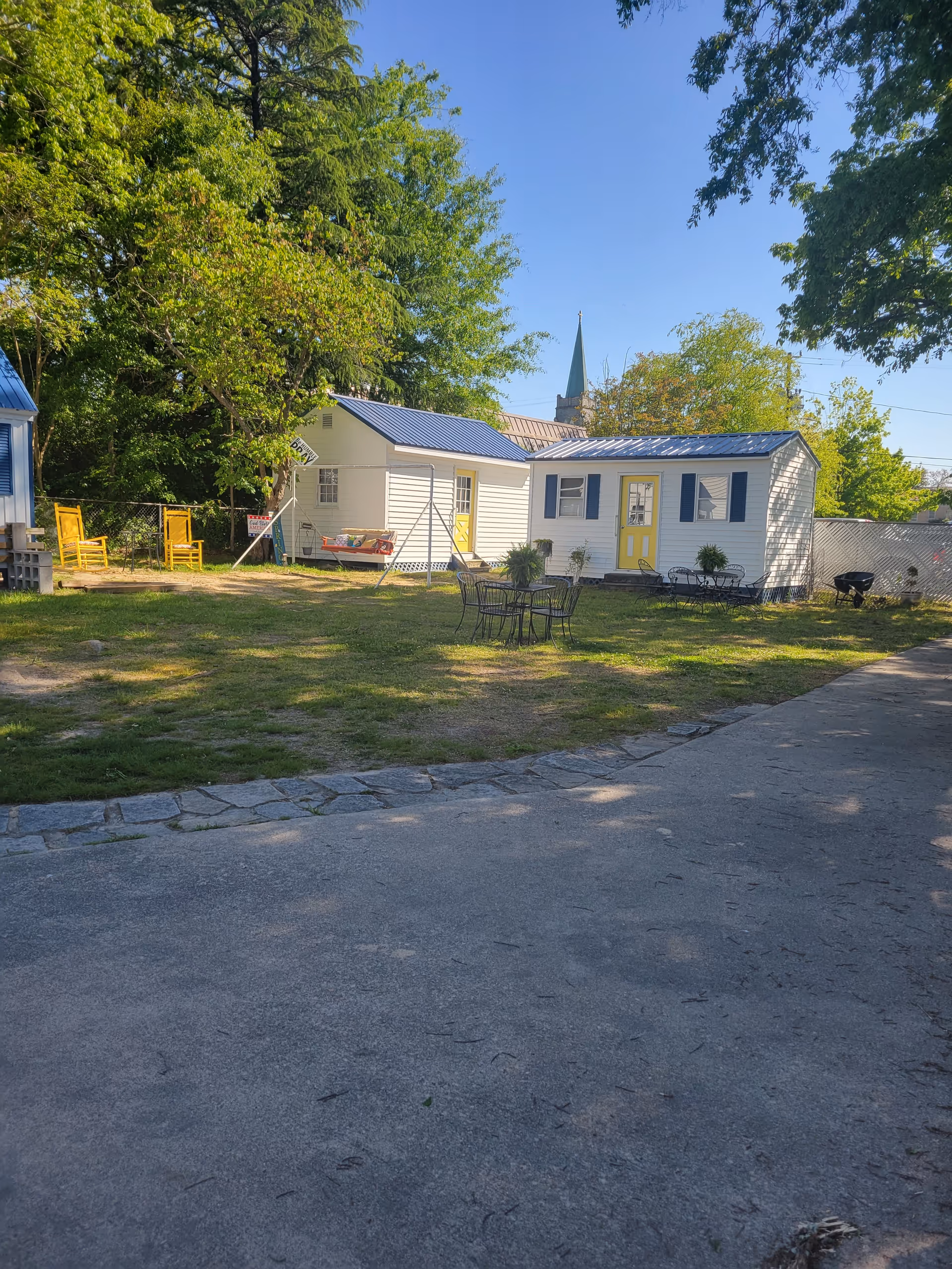 Outdoor yard with small cottages and metal chairs; blue roofs and yellow doors.