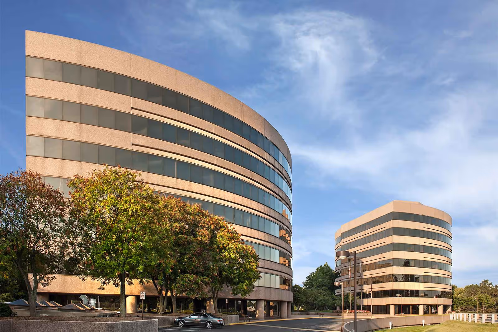 Two curved glass buildings with trees and a blue sky.