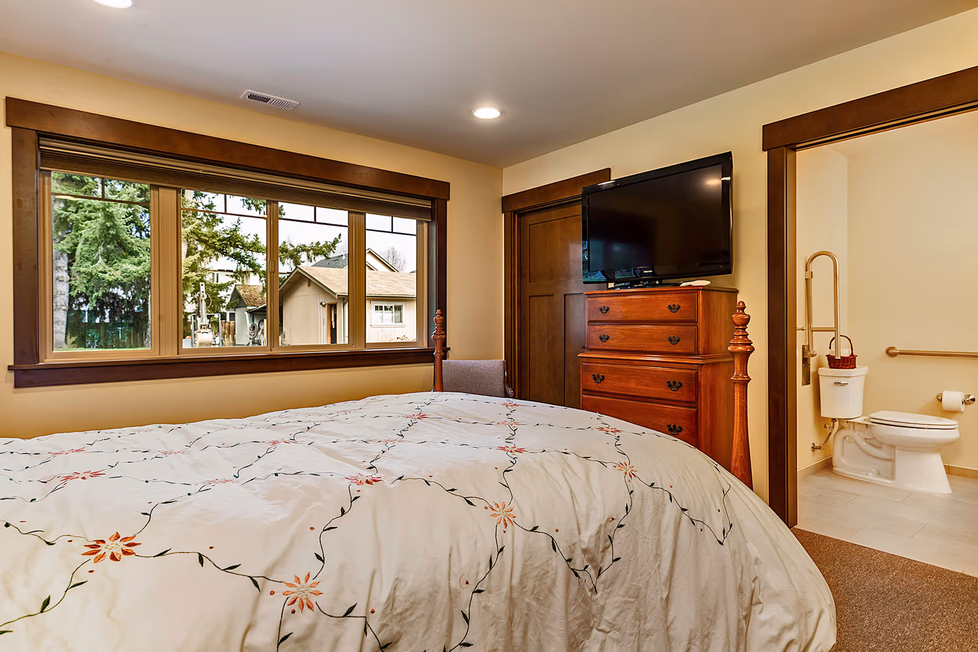 A cozy bedroom with a large bed, dresser, TV, and an open bathroom door.