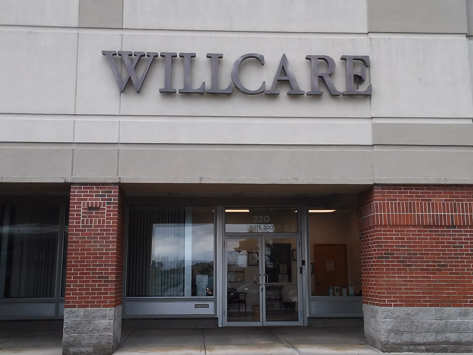 Exterior view of a WILLCARE senior living building with brick accents and glass entrance.
