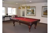 Pool table with red felt and hanging lights in a recreation room.