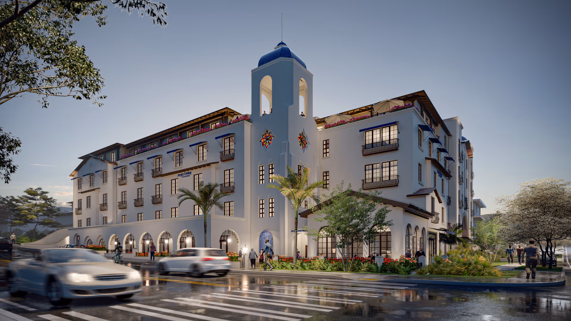 Exterior view of a multi-story senior living facility named Aegis Living San Rafael with a distinctive blue-tiled tower, palm trees, and landscaped greenery. Several people are walking on the sidewalks and cars are driving on the wet street in front of the building during dusk.