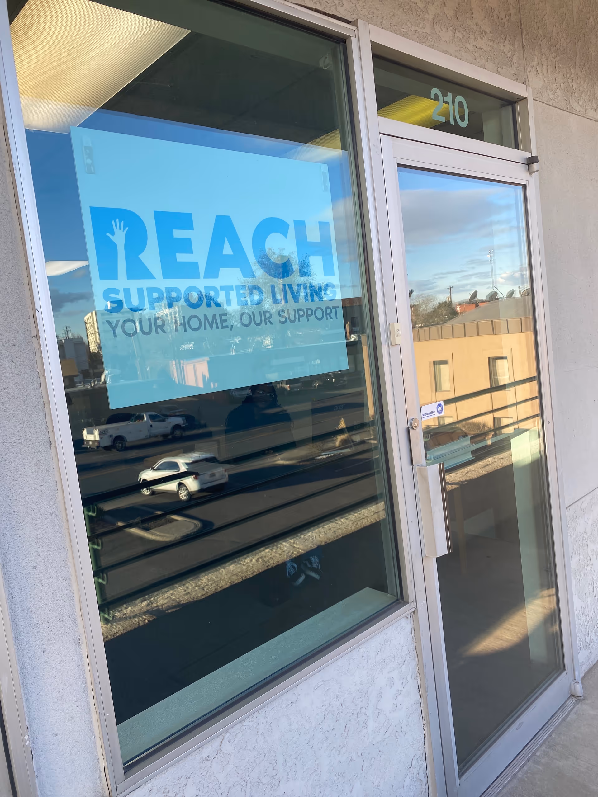 Glass door entrance with Reach Supported Living signage and reflected street outside.