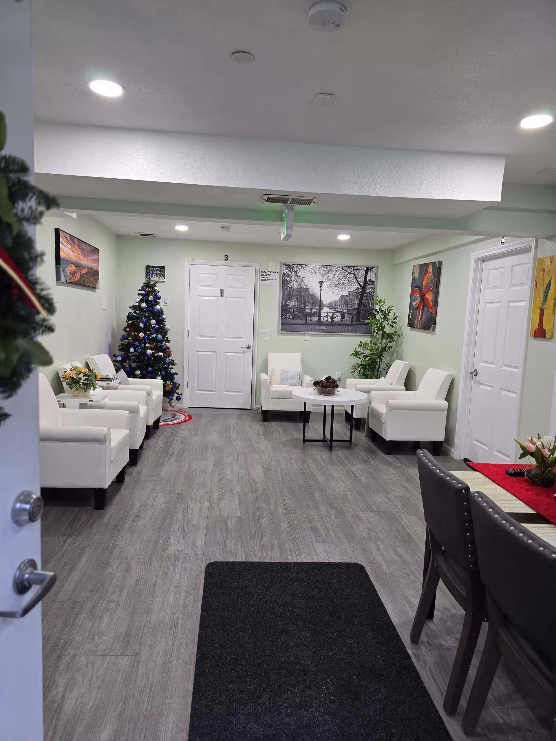 A well-lit senior living lounge with white chairs, a Christmas tree, and tables.