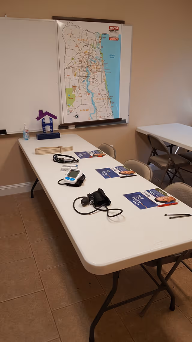 Clinic-style room with a long table, medical devices, brochures, and a wall map.
