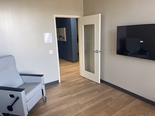 Senior living interior with a wall-mounted TV, gray walls, and a doorway.
