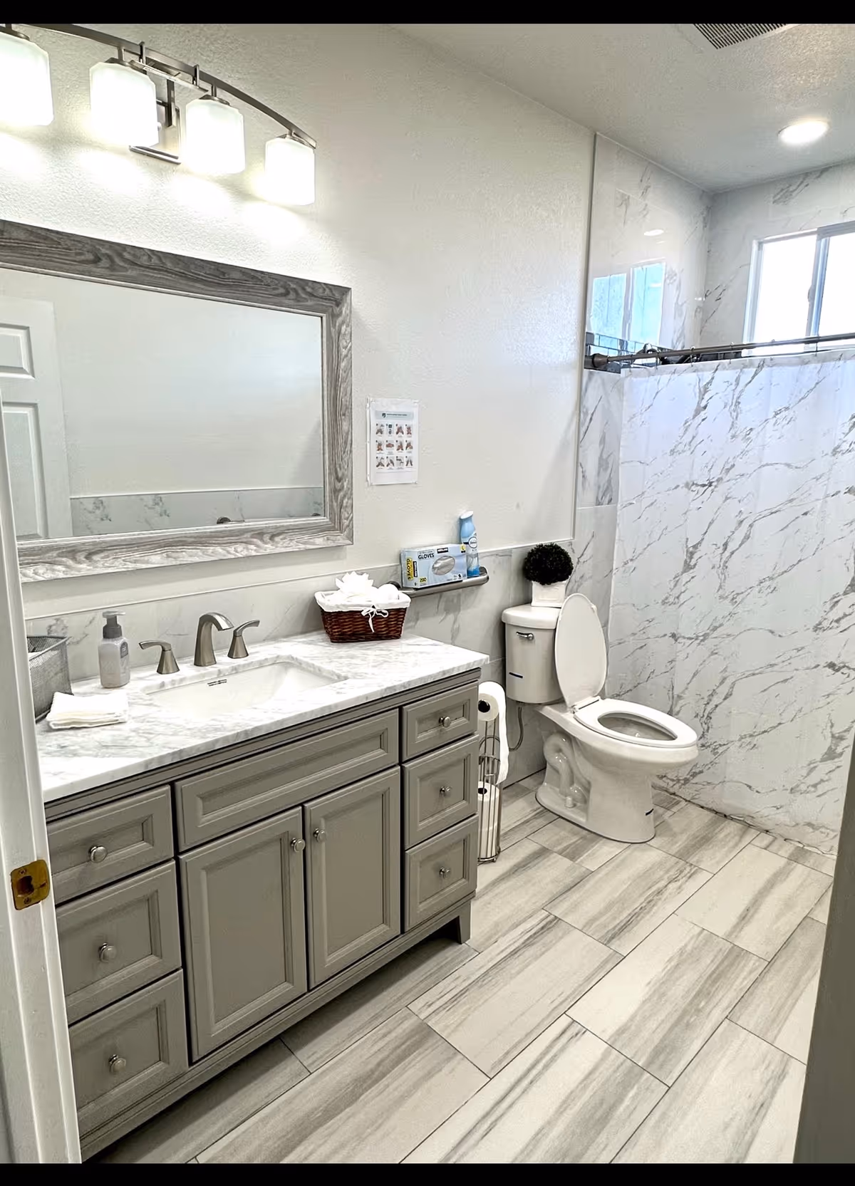 Gray marble bathroom with a vanity, mirror, toilet, and glass-enclosed shower.