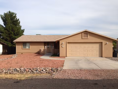 A single-story beige building with a two-car garage and desert rock landscaping.