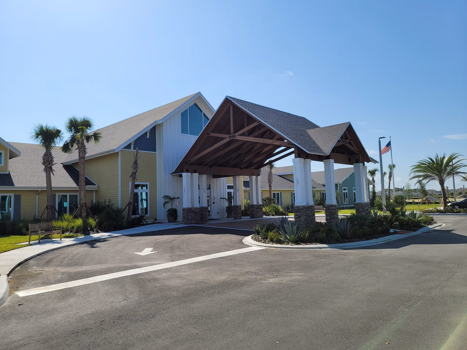 Exterior view of a senior living facility with a covered entrance and palm trees.