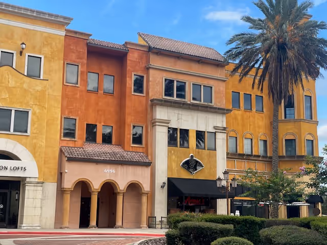 Colorful, multi-story building facade with arches and a palm tree under a blue sky.