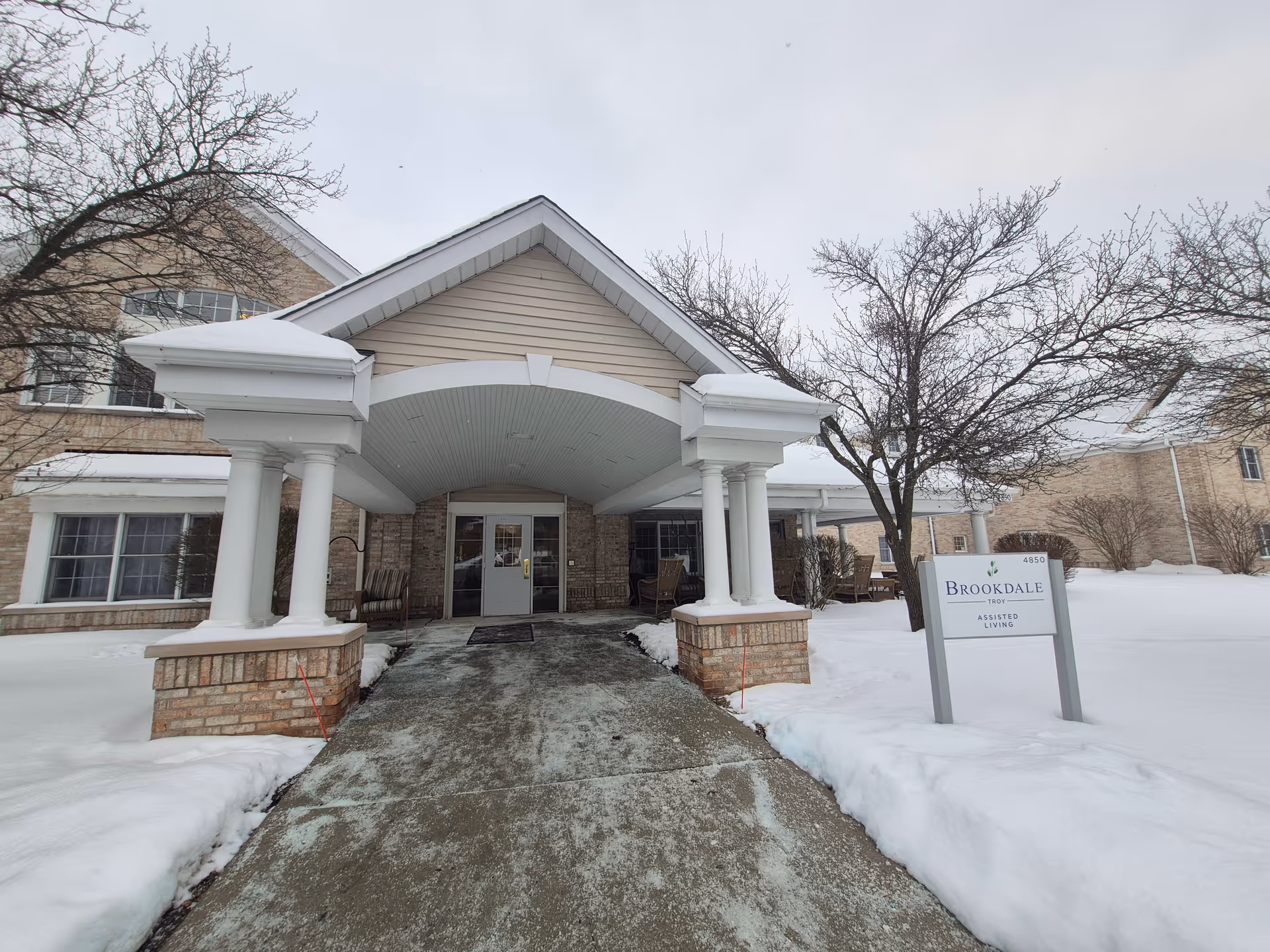 Snowy exterior of Brookdale Troy with a covered entrance and brick columns.