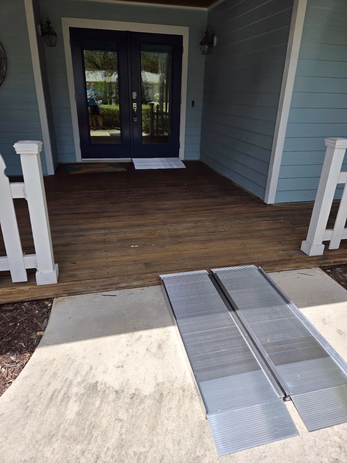 Blue double doors at a covered porch with a metal ramp leading to the entrance.