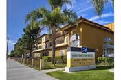 Two-story yellow Mediterranean-style senior apartments with palm trees and a Huntington Villas sign.