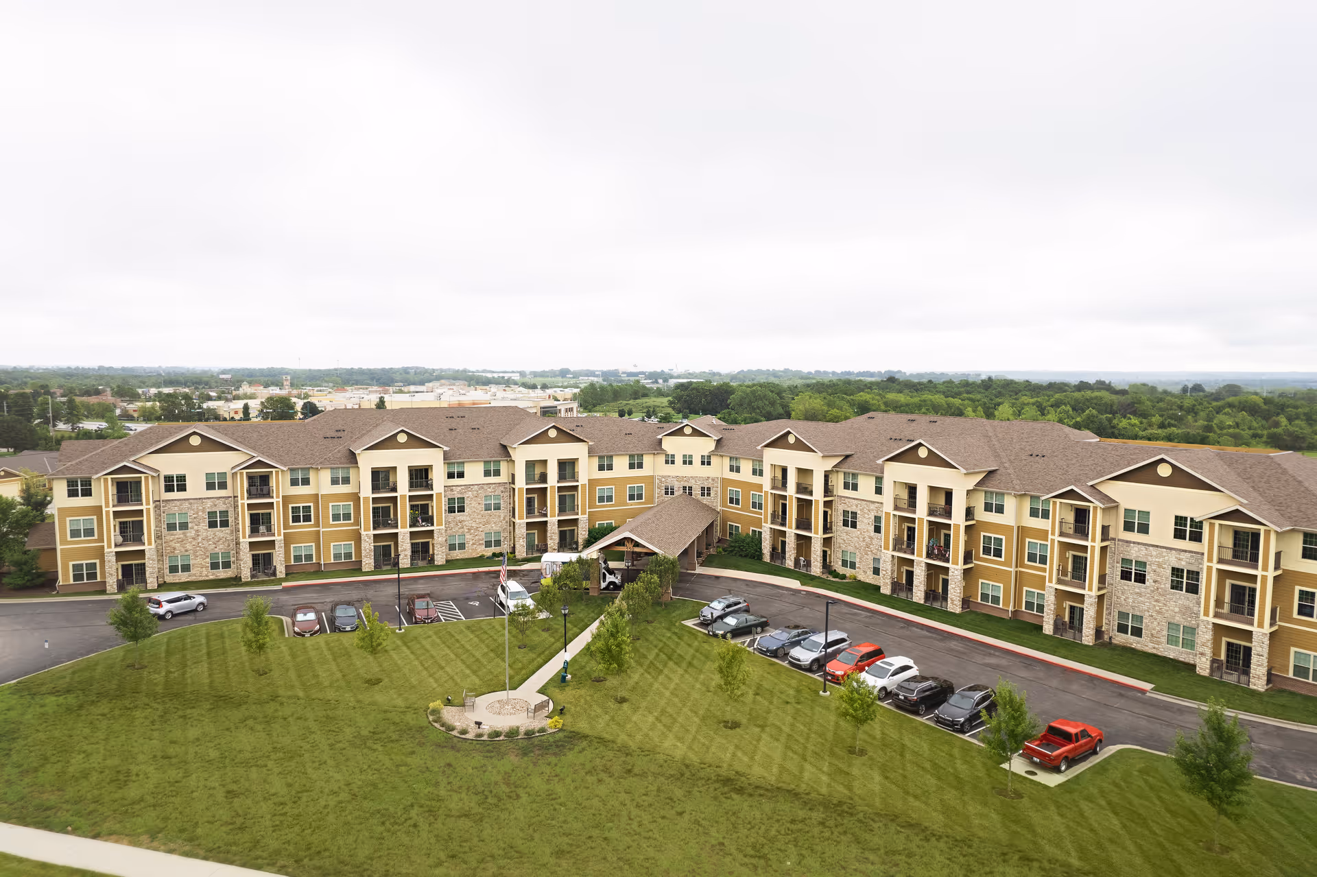 Aerial view of a large three-story senior living building with balconies, parking lot and a landscaped lawn.