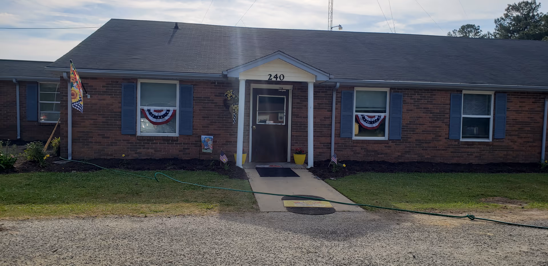 Exterior view of Pinewood Manor Assisted Living: single-story brick building with front entrance and bunting.