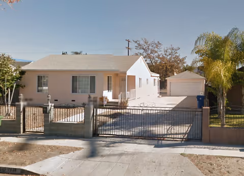 Single-story beige building with a gated front yard, driveway, and a detached garage.