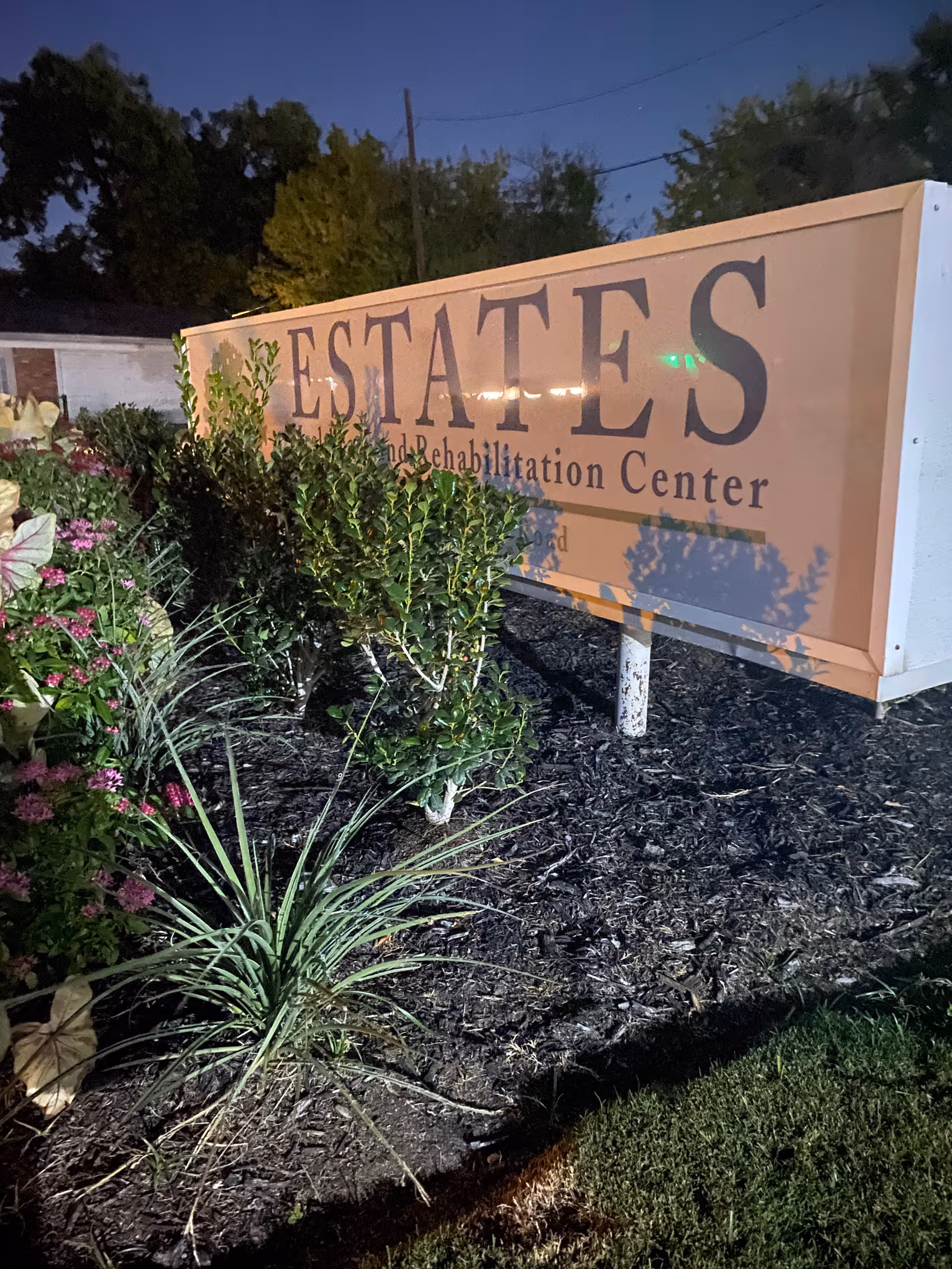 Outdoor sign for Estates Healthcare and Rehabilitation Center with shrubs and mulch in front.