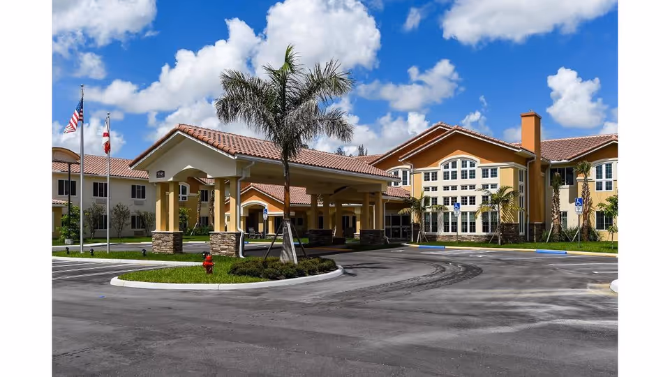 Exterior view of a senior living facility entrance with palm trees and a circular driveway.