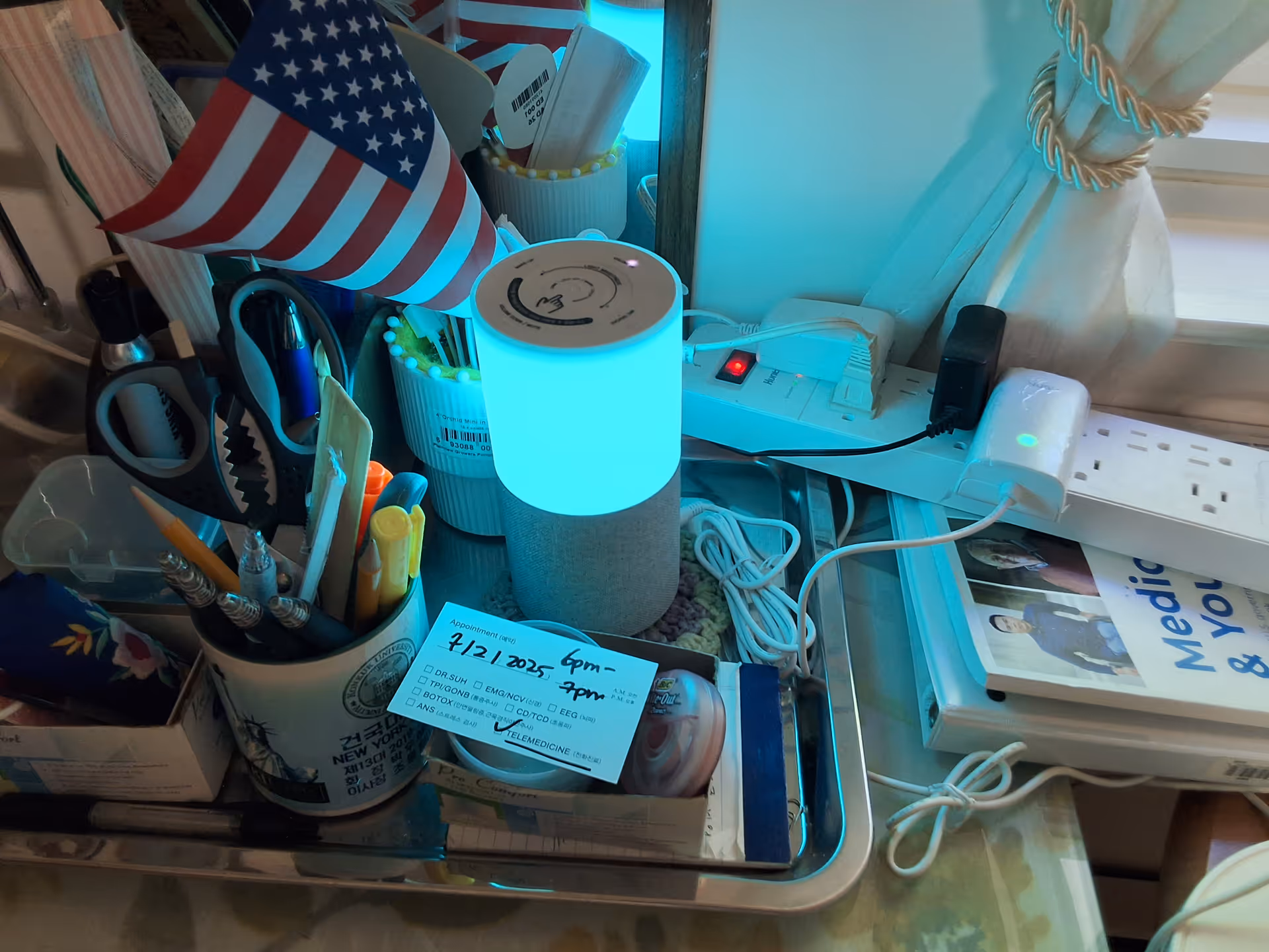 Cluttered indoor workspace with blue lamp, American flag, and various office supplies