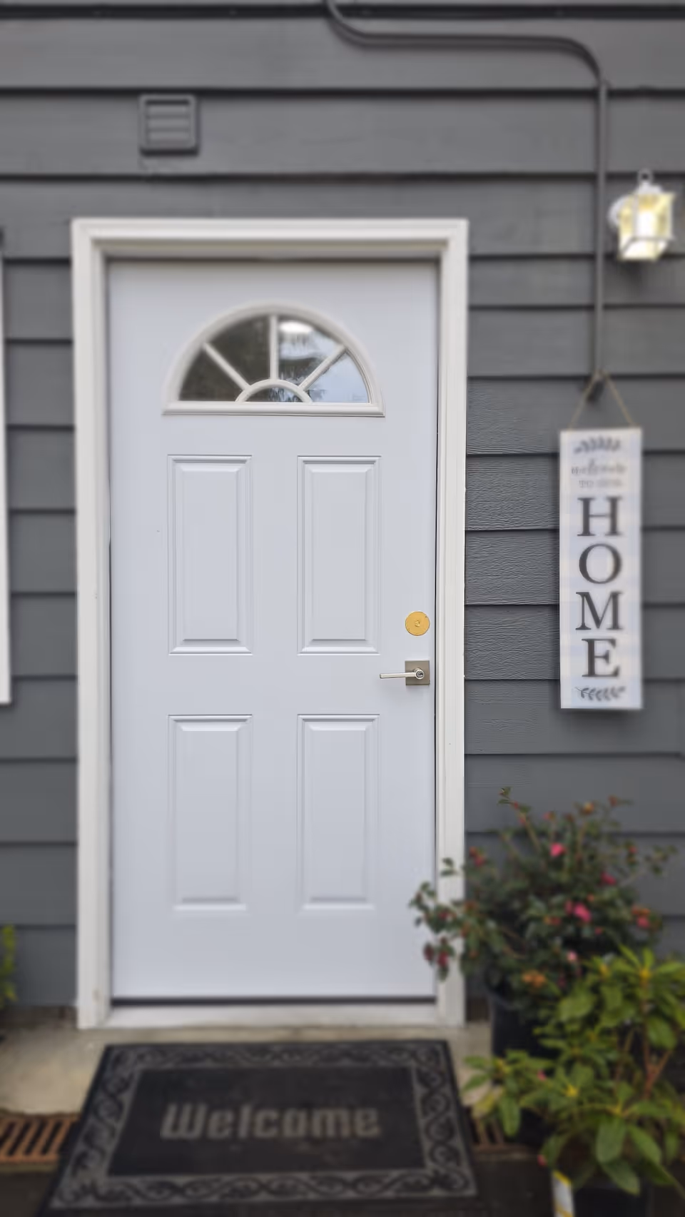 Front entrance of a gray home with a white door and welcome mat.