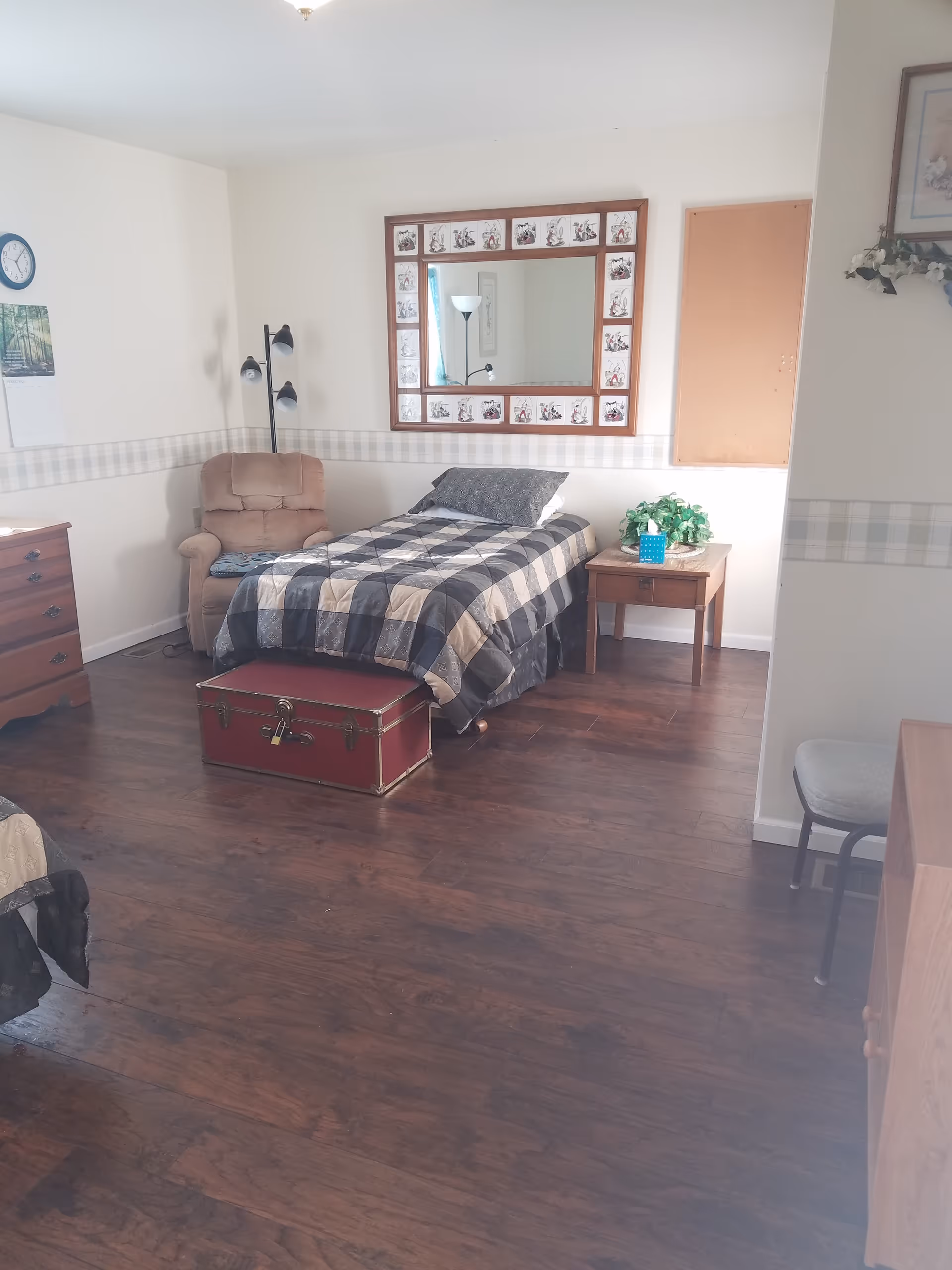 A neat senior living facility bedroom with bed, chair, side table, and mirror.