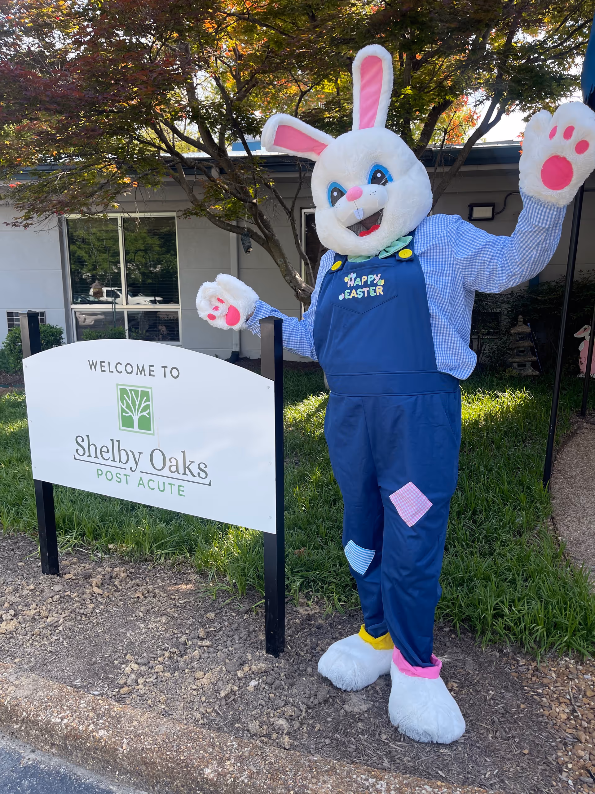 A large Easter bunny mascot stands outside a post-acute facility beside a welcome sign.