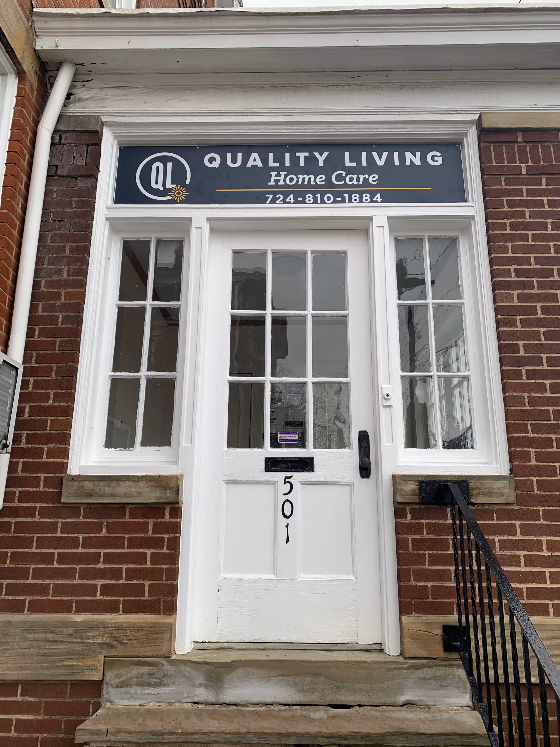 Brick building storefront with white door and sign reading Quality Living Home Care above the entrance.