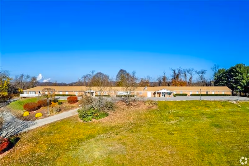 Long single-story senior living building with landscaped shrubbery and a wide grassy lawn under a clear blue sky.
