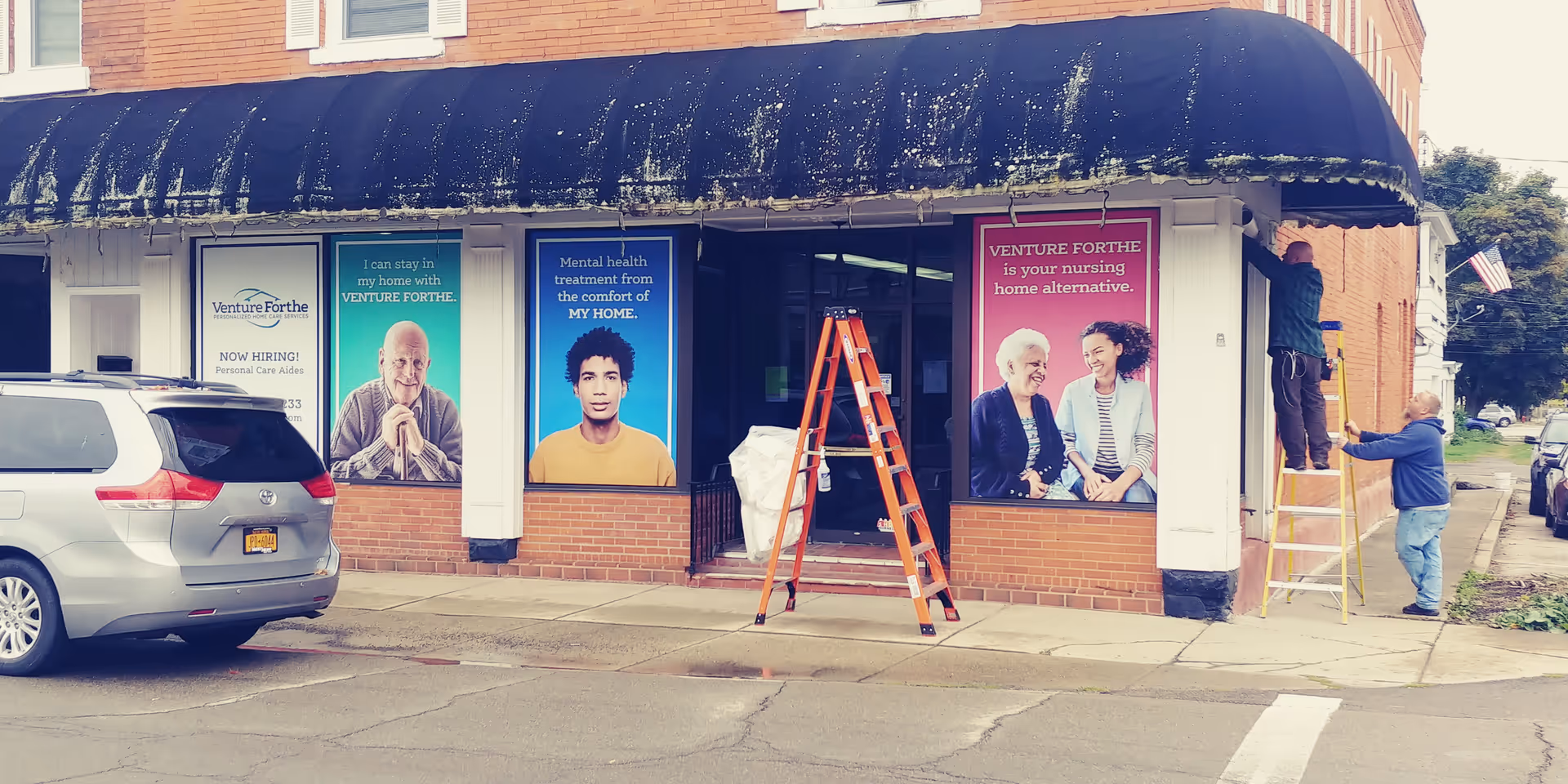 Exterior storefront of Venture Forthe Hornell Training Center with posters and workers on ladders.