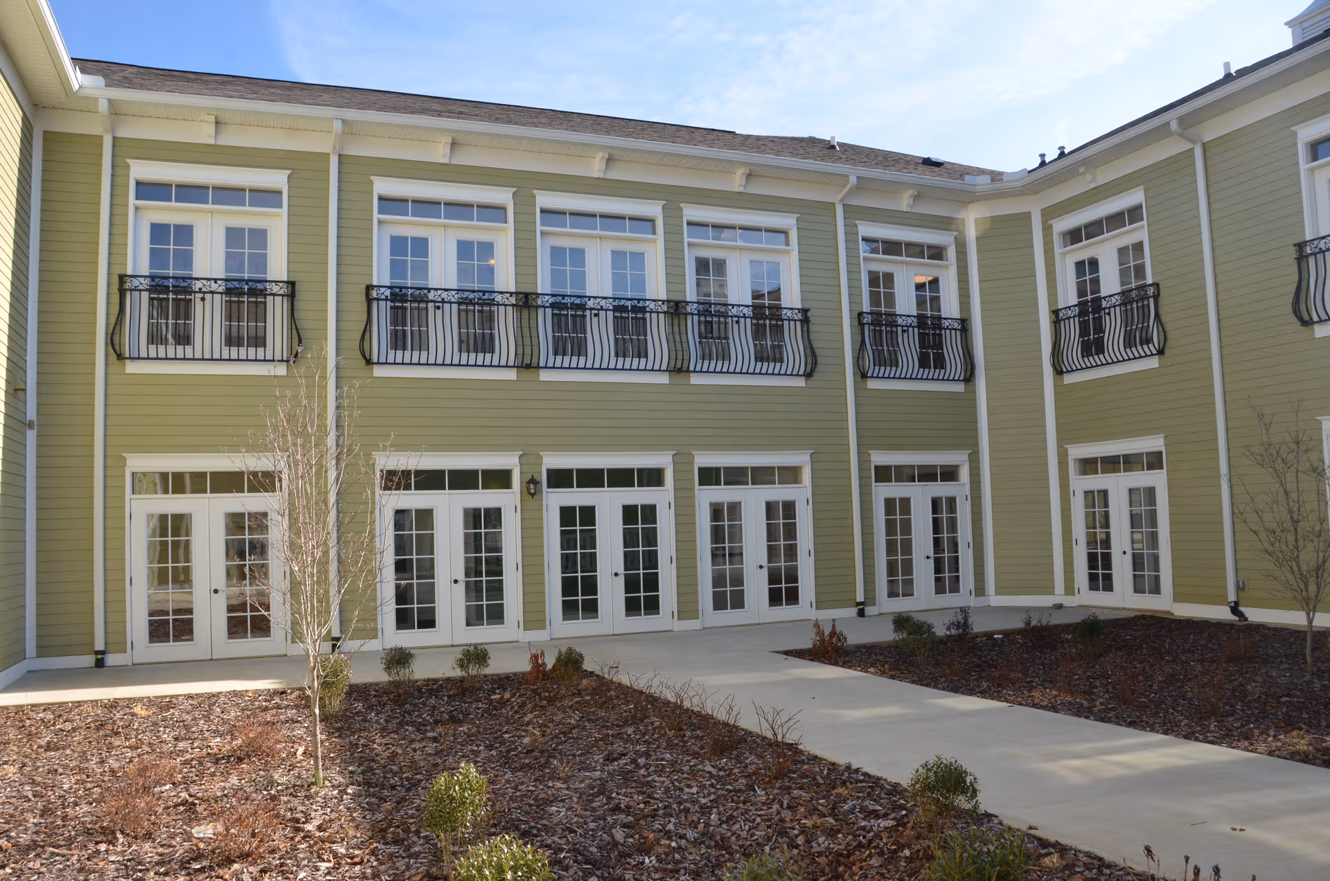 Green two-story senior living building facade with white doors and balconies.
