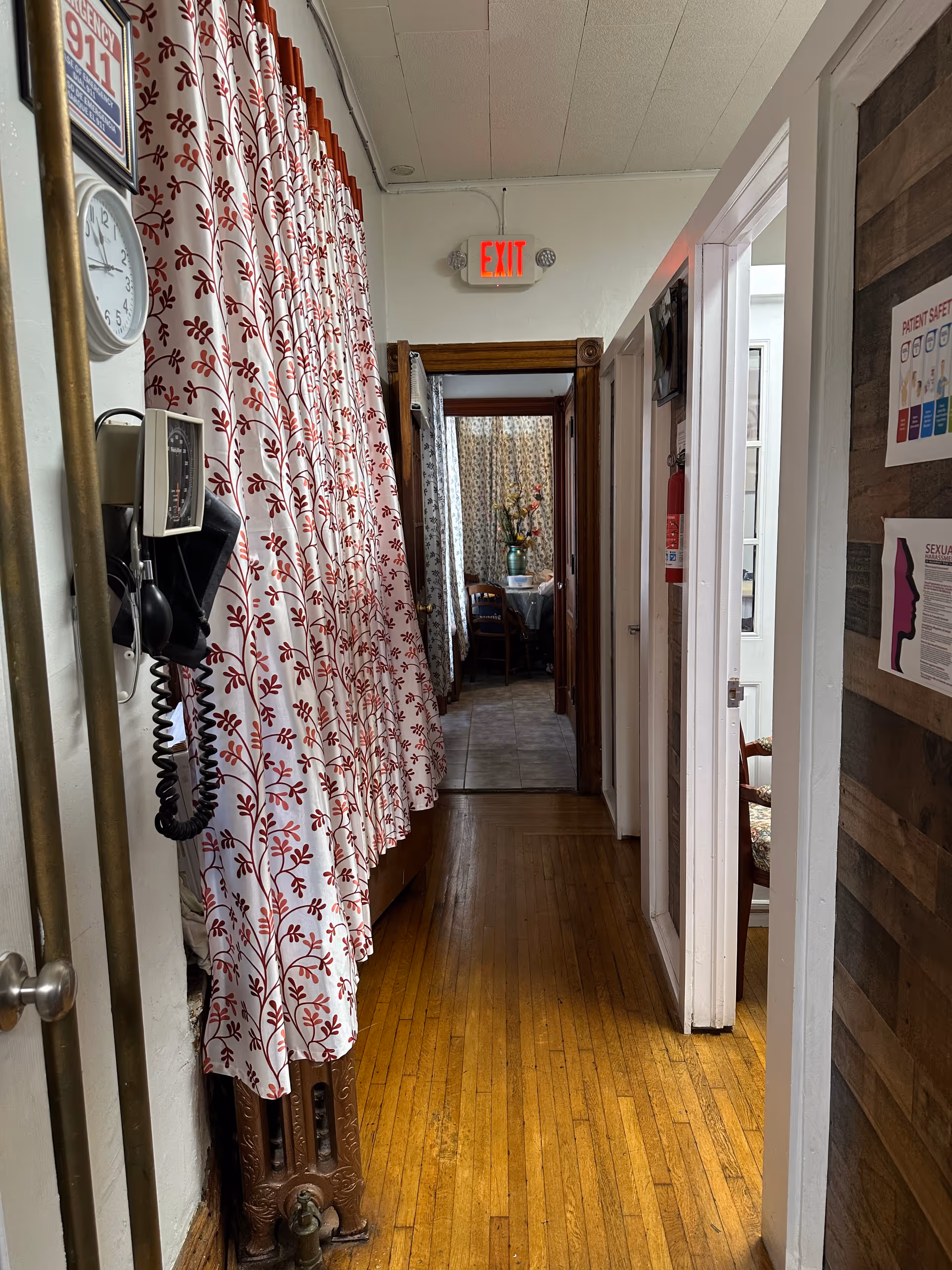 Interior hallway with red patterned curtains, wooden floor, exit sign, and doors.