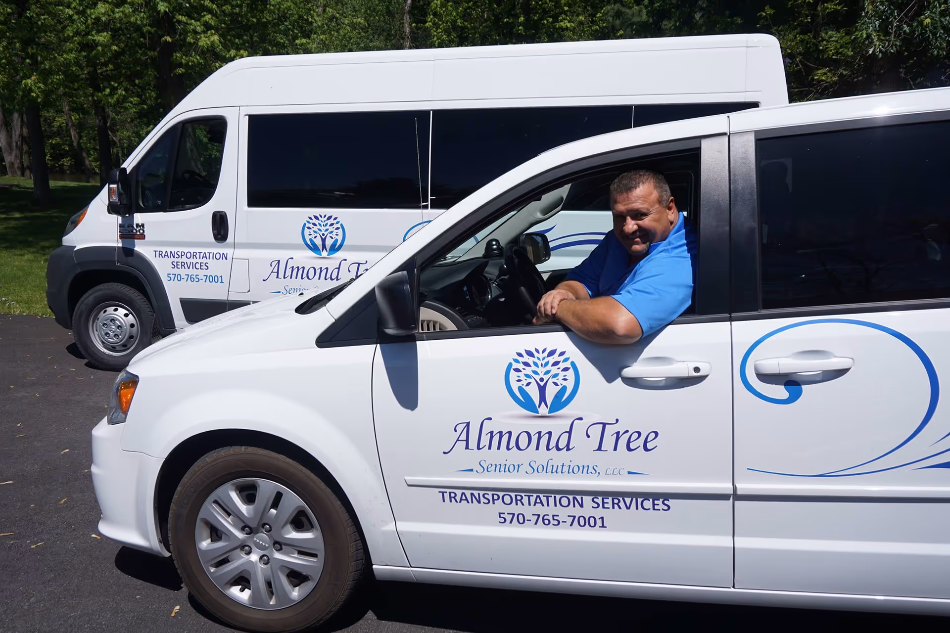Two white Almond Tree Senior Solutions vans parked with a driver visible.