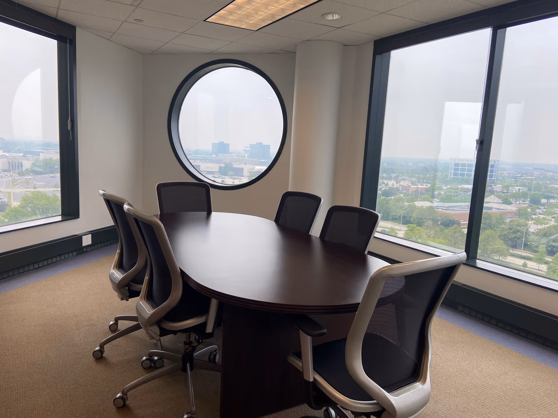 Oval table with chairs in a bright conference room by large windows.