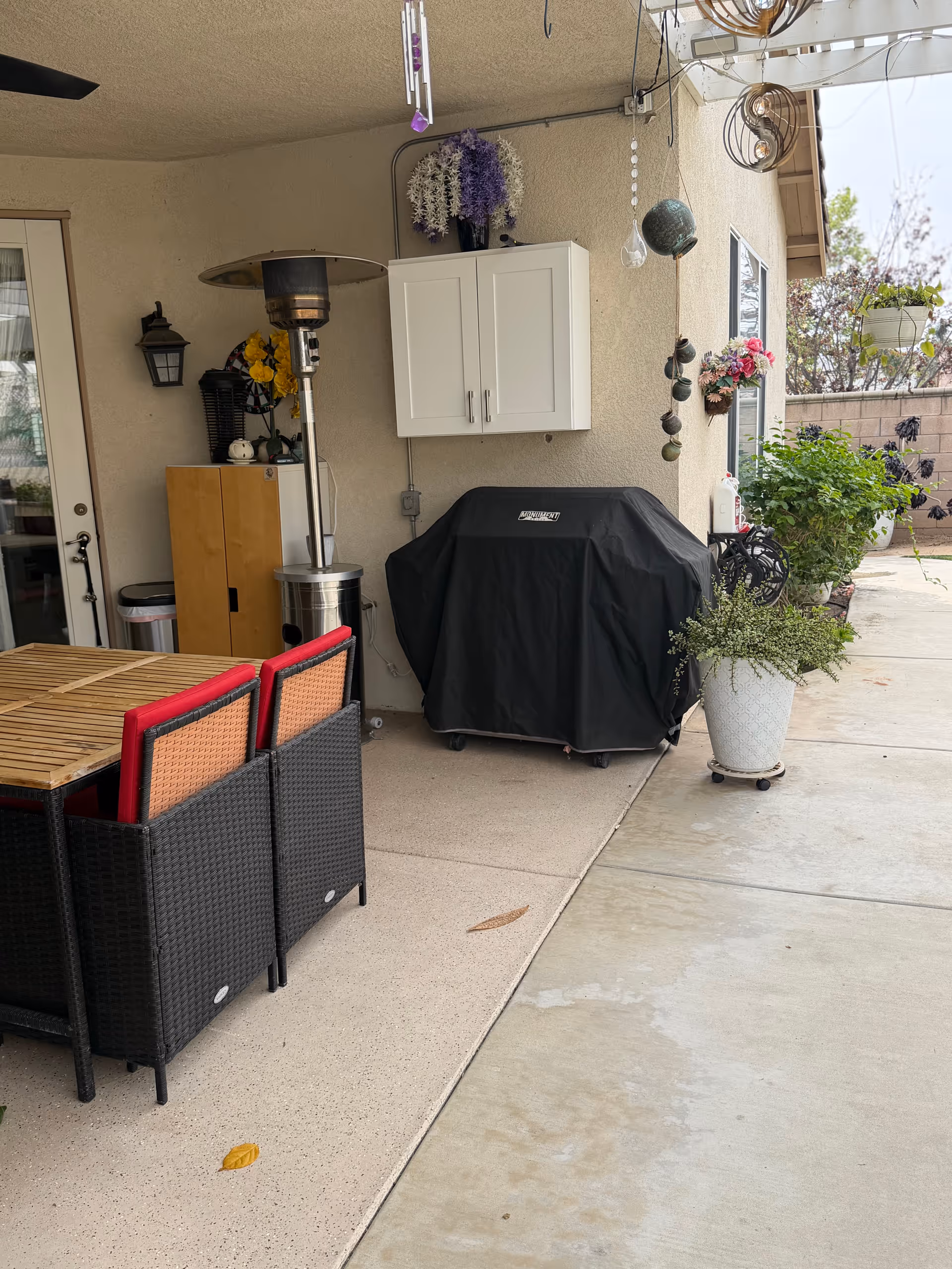 Patio dining area with a table, chairs, covered grill, and potted plants under a covered patio.